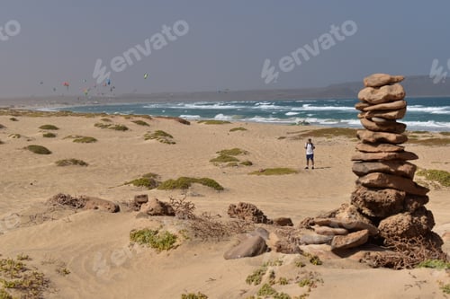 Preview: Man standing on seashore near stack of rocks