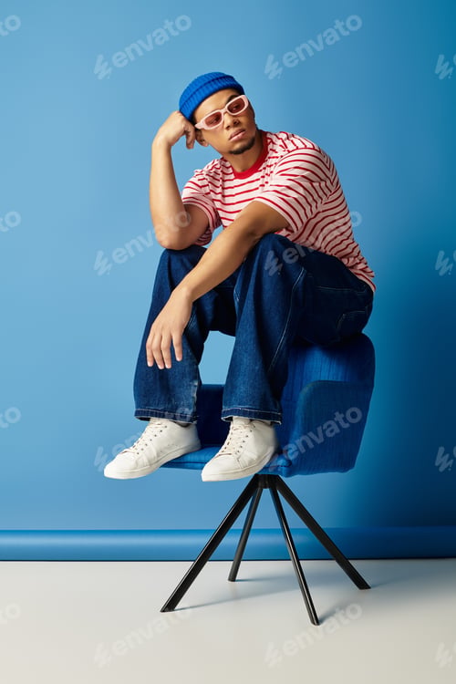 Preview: Trendy young African American man poses stylishly against a blue backdrop