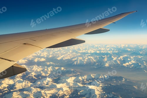 Preview: Wing of plane over mountain cover with white snow. Airplane flying on blue sky. Scenic view