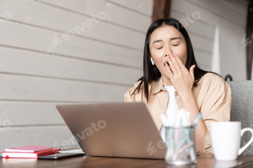 Preview: Tired girl student working on laptop and yawning, drinking coffee while studying, doing homework on