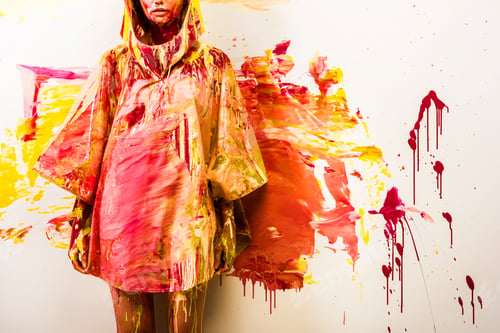 Preview: cropped image of woman standing in raincoat painted with yellow and red paints near wall