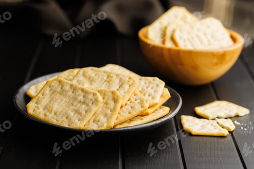 Preview: Salted Crackers on Black Plate Against a Dark Background