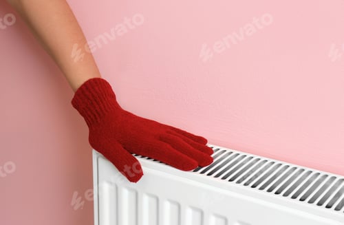 Preview: Woman in glove warming hand on heating radiator near color wall