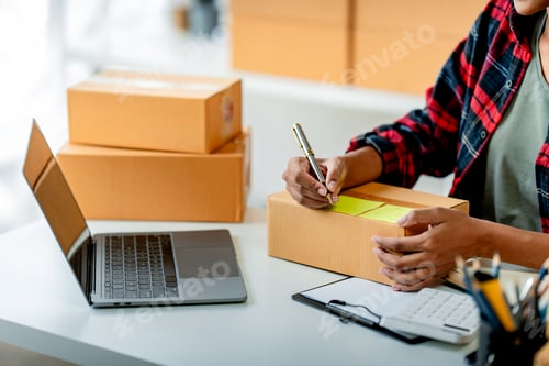 Preview: Young African woman prepares parcel boxes and checks online orders for delivery to customers on lapt