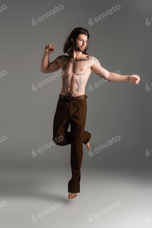 Preview: Shirtless and tattooed man jumping on grey background