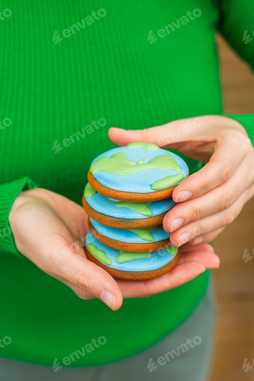 Preview: Earth Day concept. Stack of cookies in the shape of the Earth in female hands.