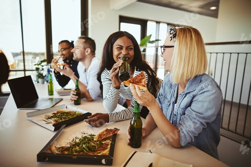 Preview: Two smiling businesswomen talking over beers and pizza after work