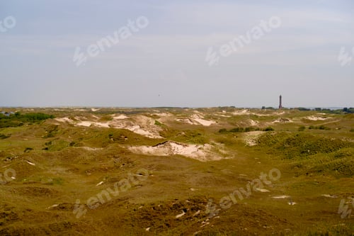 Preview: Wide view of rolling sand dunes with a distant lighthouse under a clear sky. North Sea, Germany