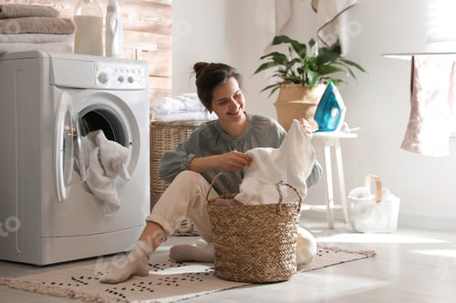 Preview: Young woman with laundry basket near washing machine at home