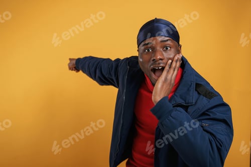 Preview: showing something by hand on the wall. Handsome black man is in the studio against yellow background