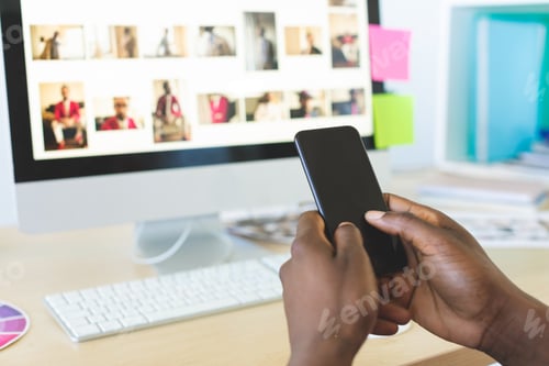 Preview: Rear view of young African-American graphic designer using mobile phone at desk in office