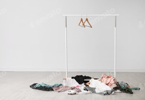 Preview: Wardrobe rack with hangers and pile of clothes on floor indoors. Space for text