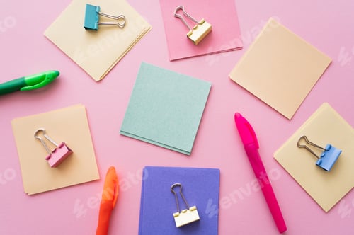 Preview: flat lay of fold back clips on colorful paper notes near pens on pink