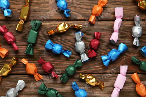 Preview: Many candies in colorful wrappers on wooden table, flat lay
