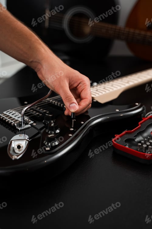 Preview: Hand turns volume knob on glossy black electric guitar for tone refinement