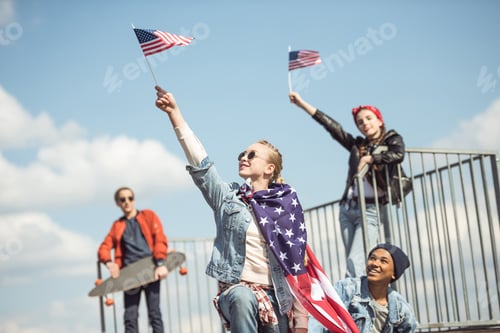 Preview: Teenagers group having fun together and waving american flags at skateboard park