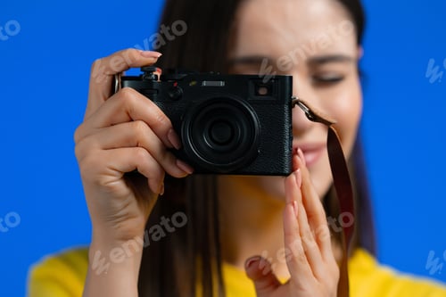 Preview: Young pretty woman takes pictures with DSLR camera over blue background in studio. Girl smiling as p