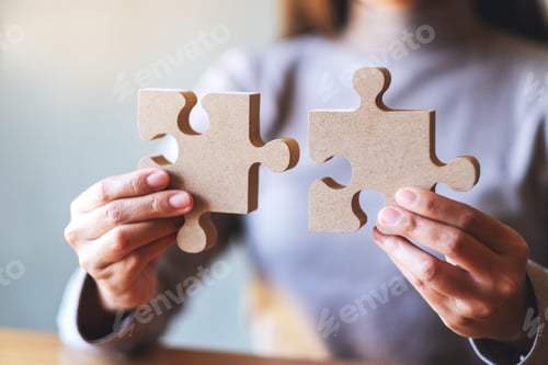 Preview: Closeup image of a woman holding and putting a piece of wooden jigsaw puzzle together