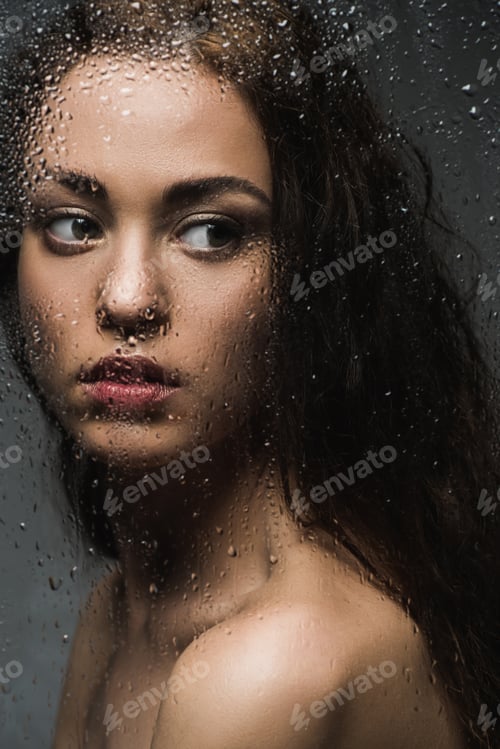 Preview: attractive brunette woman behind wet glass in shower