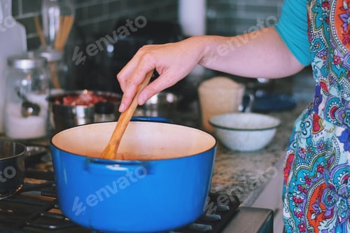 Preview: Woman is cooking dinner in a blue cast iron pot, Dutch oven, on a stove