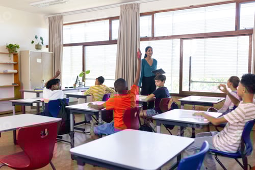 Preview: In school, Indian female teacher holding tablet and students raising hands in classroom