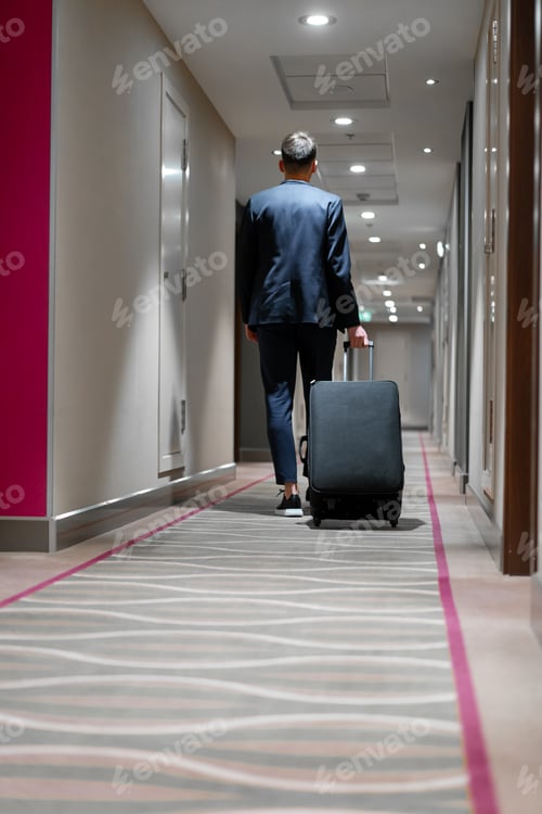 Preview: A man with a suitcase walks down the hotel corridor a back view of a businessman on trip