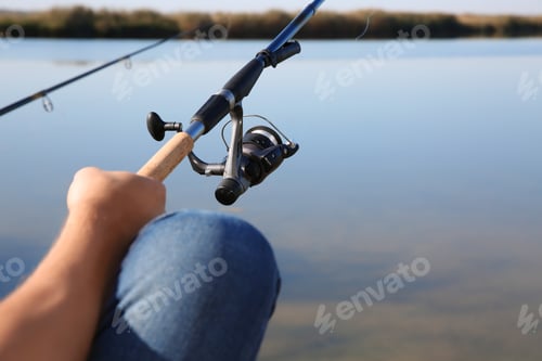 Preview: Man fishing alone at riverside on sunny day, closeup