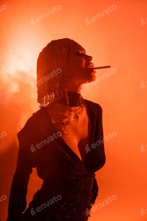 Preview: seductive tattooed woman in metallic wig and black sexy dress posing with cigarette on red and