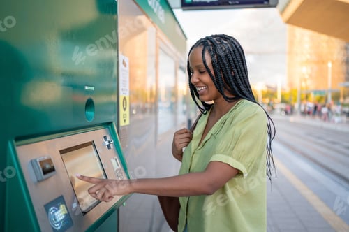 Preview: Young woman buying train ticket at self-service machine