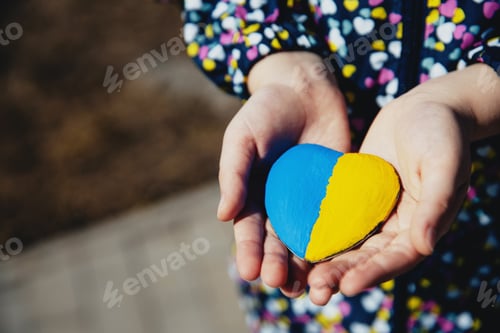 Preview: Small little kid hold heart shaped stone with Ukraine national flag or anthem