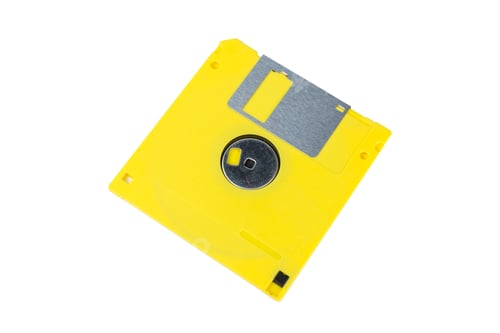 Preview: Old yellow floppy disk on white background with metal sliding cover showing storage technology