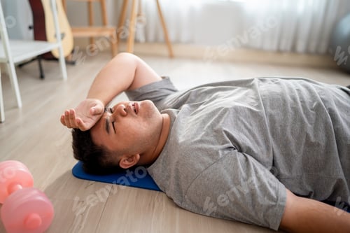 Preview: Exhausted Asian plus-size man lying down on a yoga mat after workout.