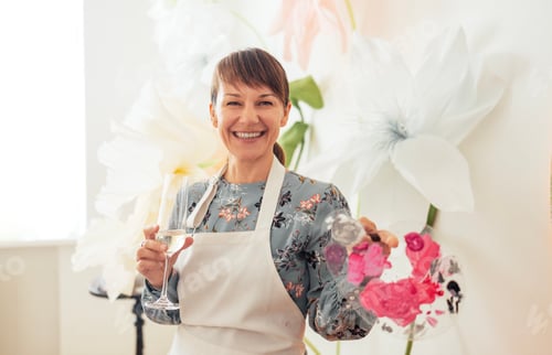 Preview: A young woman in a dress and apron holds a glass of champagne and a palette with paint