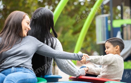 Preview: Happy family having fun spinning on merry go round at playground