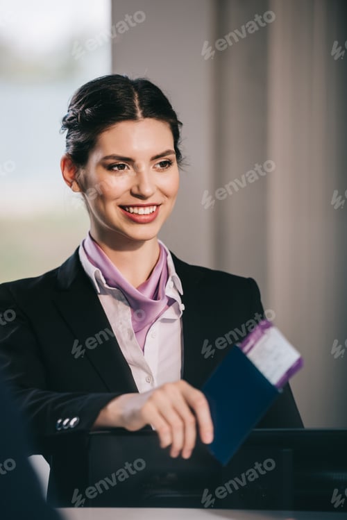 Preview: beautiful smiling young airport worker holding passport with boarding pass at check-in desk
