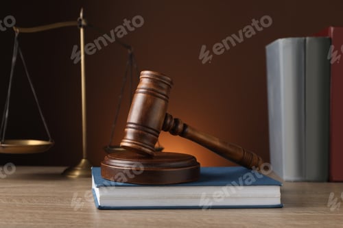 Preview: Judge's gavel with sound block, scales of justice and books on wooden table against brown background
