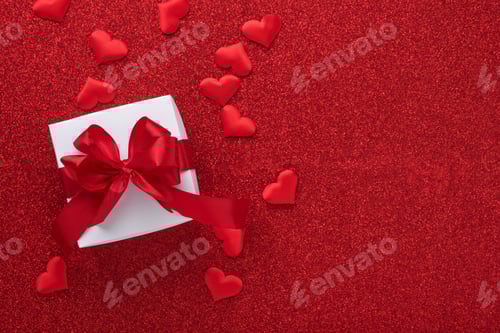 Preview: White gift boxes with red ribbon and small red decorative hearts on red background. Top view with co
