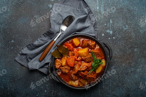 Preview: Beef meat stew with potatoes, carrot and delicious gravy in black casserole pot with bay leaves and