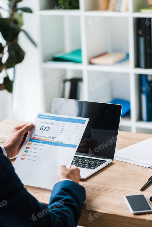Preview: cropped view of man holding paper with credit report letters near laptop