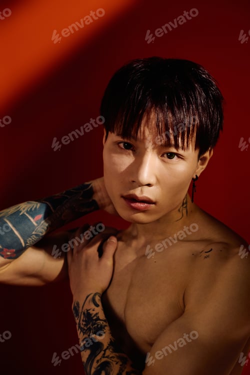 Preview: Handsome young man with tattoos posing against a vibrant red background