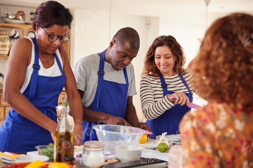 Preview: Male And Female Adult Students With Teacher Preparing Ingredients For Dish In Kitchen Cookery Class