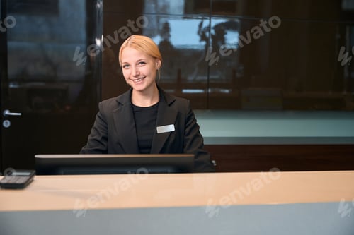 Preview: Young smiling european female receptionist at reception desk in hotel lobby