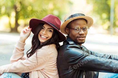 Preview: Smiling interracial couple in hats sitting back to back