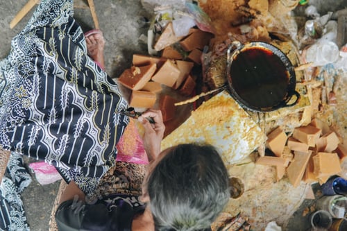 Preview: Top view of a person's hand drawing the design pattern of Indonesian batik tulis fabric.