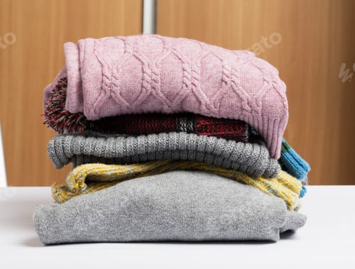 Preview: Stack of clean folded clothes on white table, help and volunteering concept