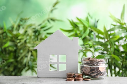 Preview: House model and jar with coins on table against blurred background. Space for text
