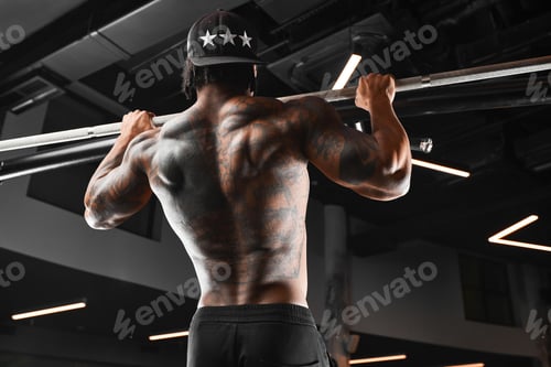 Preview: Strong and muscular dark skin man trains on modern equipment in gym. Portrait of muscular pumped up