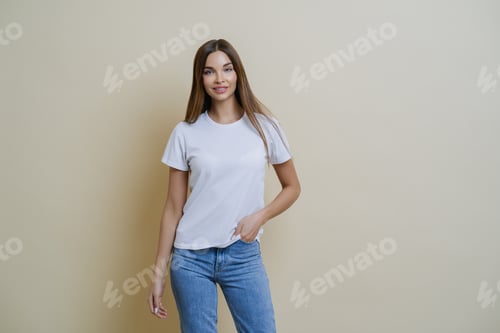 Preview: Woman keeps hand in pocket, wears casual t shirt and jeans, stands in relaxed pose.