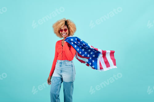 Preview: Young woman smiling while holding a US flag on an isolated background.
