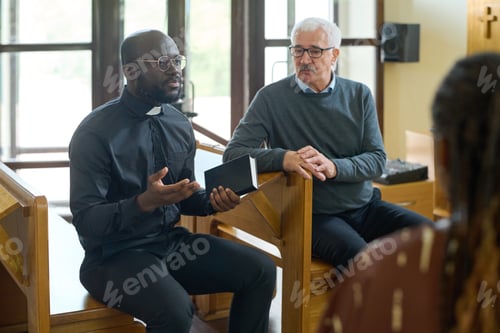 Preview: Confident pastor in black shirt with clerical collar explaining verses from Bible